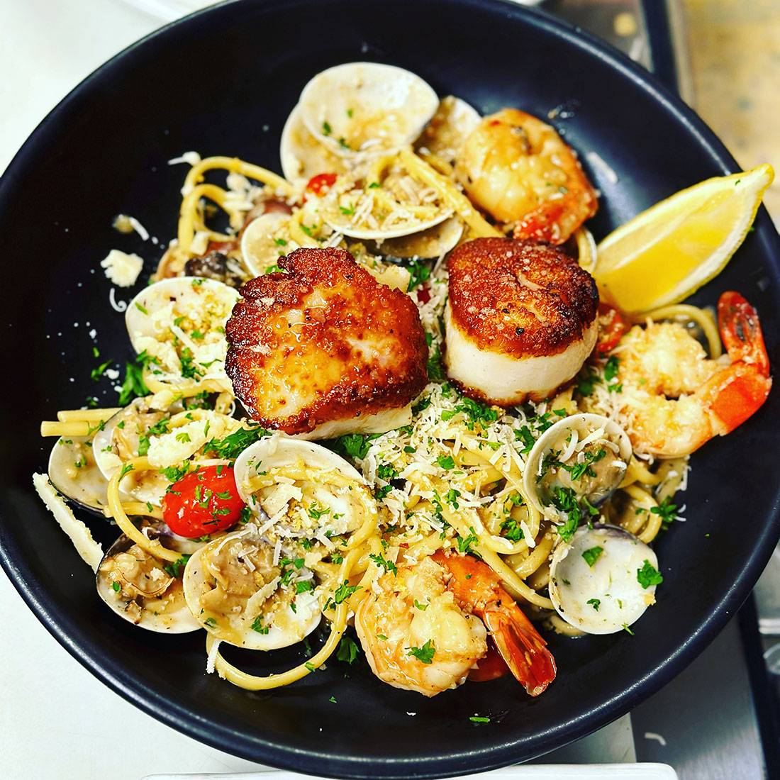 Seafood pasta served with a lemon wedge on a black plate