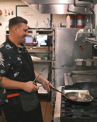 Seasoning Bistro chef and co-owner cooking steak on stove with a smile