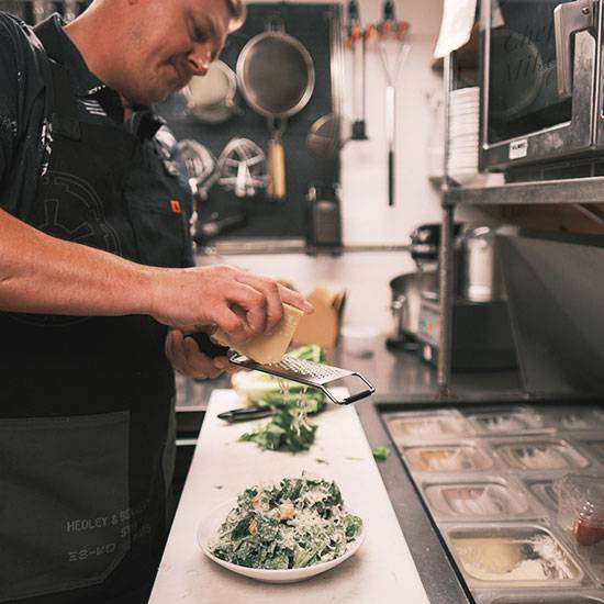 Seasoning chef and co-owner grating fresh parmesan over Cesar salad