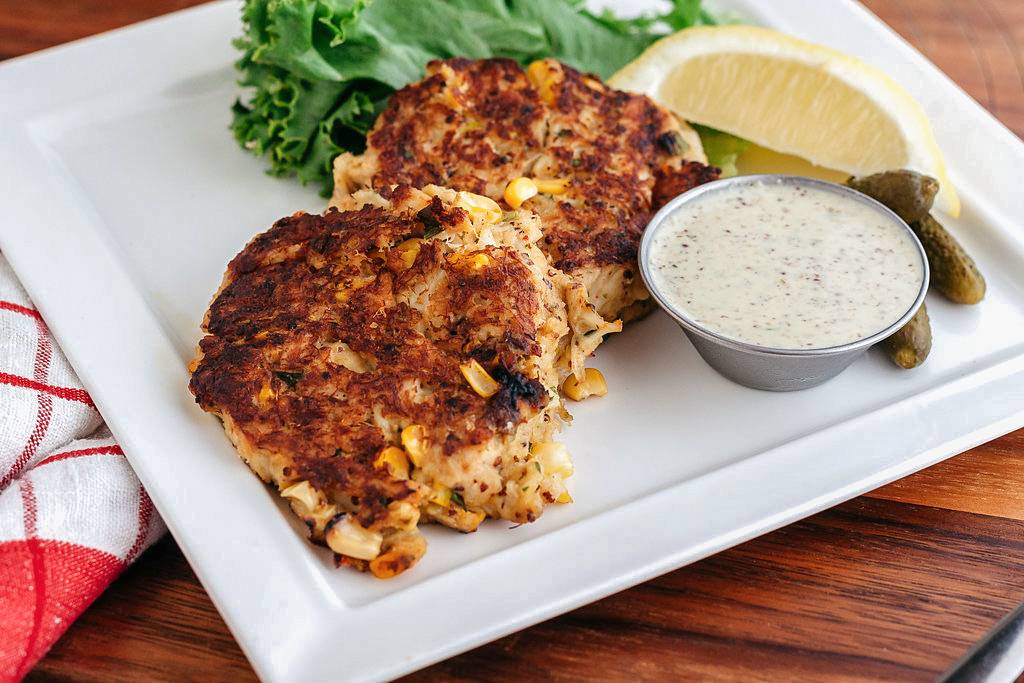 Close up of crab cakes served with sauce and cornichons